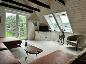 Une pièce avec un lit en mezzanine, un canapé, une table basse en bois, un téléviseur posé sur un meuble et une statue de cerf.