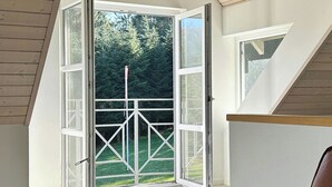 Puerta abierta que da a un balcón con vistas a árboles y un área verde.