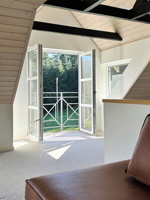 Une porte ouverte donnant sur un balcon avec vue sur des arbres et une zone herbeuse.