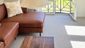 Una habitación con un sofá de cuero marrón, una mesa de centro de madera, una lámpara colgante y vistas a un paisaje verde a través de una puerta de cristal.