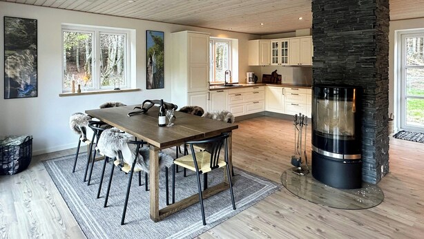 Una cocina moderna con armarios blancos, una chimenea de piedra y un comedor con mesa y sillas de madera.