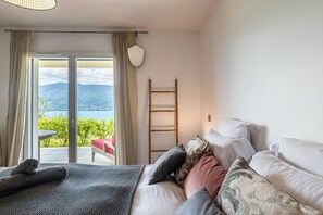 Ein Schlafzimmer mit Bett, Kissen, einer Leiter und Blick auf einen Balkon mit Tisch und Stuhl.