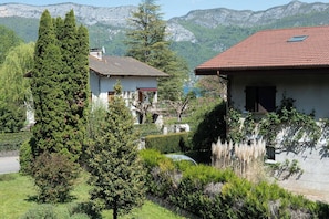 Ein Wohngebiet mit zwei Häusern, eines mit rotem Dach und das andere mit weißer Fassade, umgeben von üppiger Vegetation und Bergen im Hintergrund.