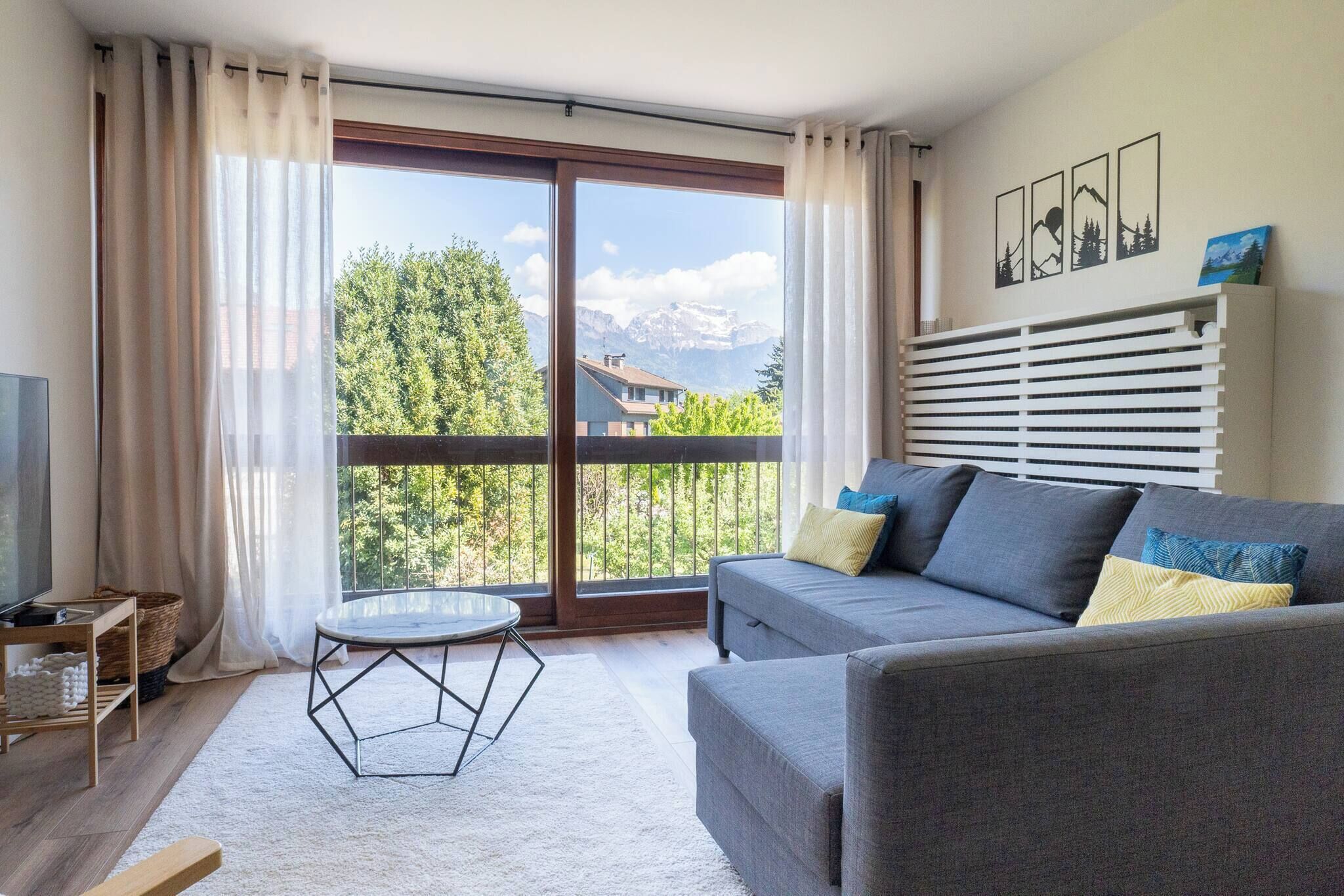 A modern living room with a sofa, a glass coffee table, and a view of mountains through large windows.