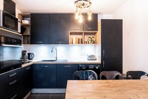 Eine moderne Küche mit dunklen Schränken, einer Holz Arbeitsplatte, einem eingebauten Geschirrspüler und einem Essbereich mit Holztisch und Stühlen.