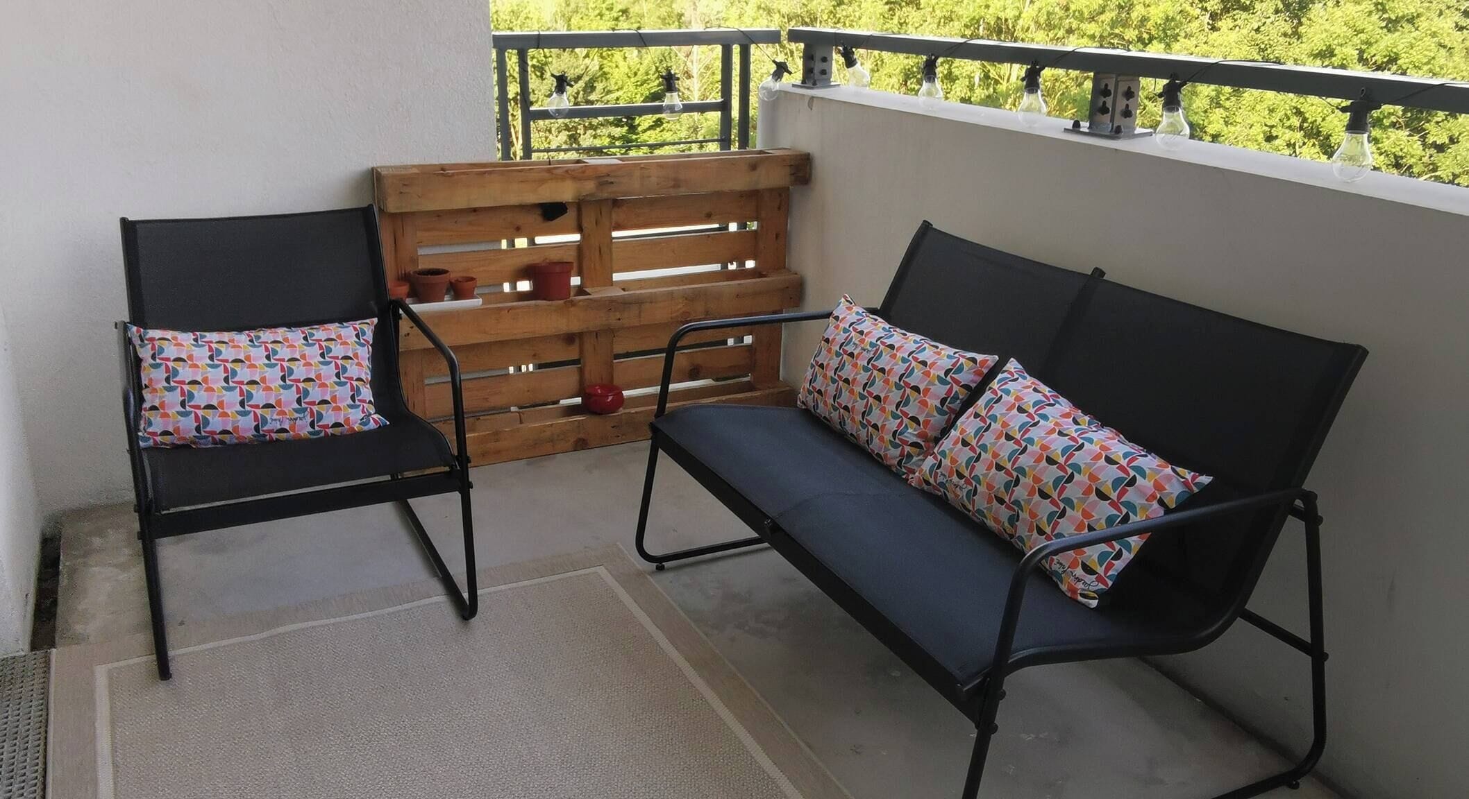 Un balcón con dos sillas, un sofá, listones de madera y lámparas colgantes.
