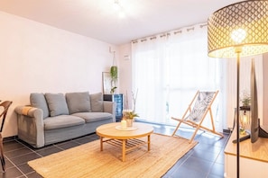 Ein Wohnzimmer mit grauem Sofa, rundem Couchtisch, einer hängenden Pflanze und einer Stehlampe.