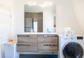 Ein modernes Badezimmer mit integrierter Waschmaschine, einem Spiegel und einem hölzernen Waschtisch.