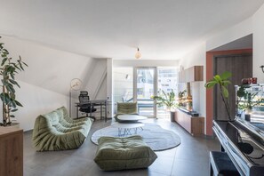 Ein modernes Wohnzimmer mit einer Couch, einem Couchtisch und einem Fernseher. Pflanzen und eine Treppe sind sichtbar.