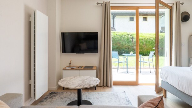 Ein modernes Hotelzimmer mit Bett, Fernseher, kleinem Tisch und einer Schiebetür zu einem Balkon.