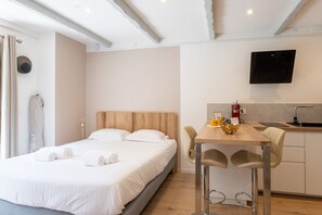 A hotel room with a bed, a desk, a chair, a TV, and a kitchenette. - - (Annecy)