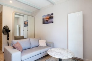 A modern living room with a grey sofa, a round marble coffee table, a large mirror, and a painting of a sunset over water. - - (Annecy)