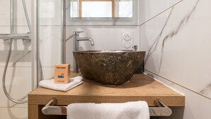 Ein Badezimmer mit Marmorwand, einem hölzernen Waschtisch, einem großen Steingefäß, einem Handtuch und einer Willkommensbox.