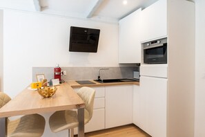 A compact kitchen with a built-in oven, a wall-mounted air conditioner, and a wooden dining table with chairs. - - (Annecy)