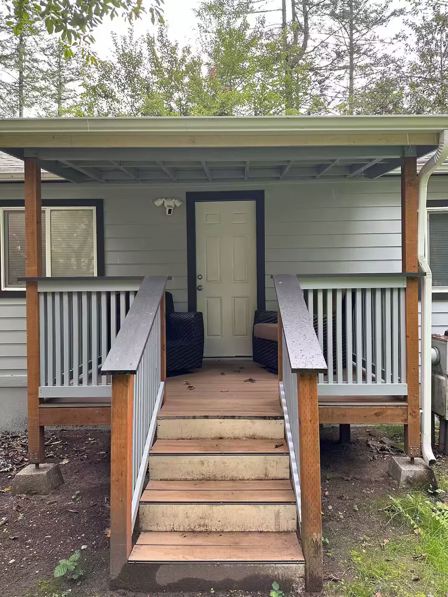 A covered porch with a wooden staircase leading to a door, surrounded by railings and a small garden area.