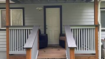 A covered porch with a wooden staircase leading to a door, surrounded by railings and a small garden area.
