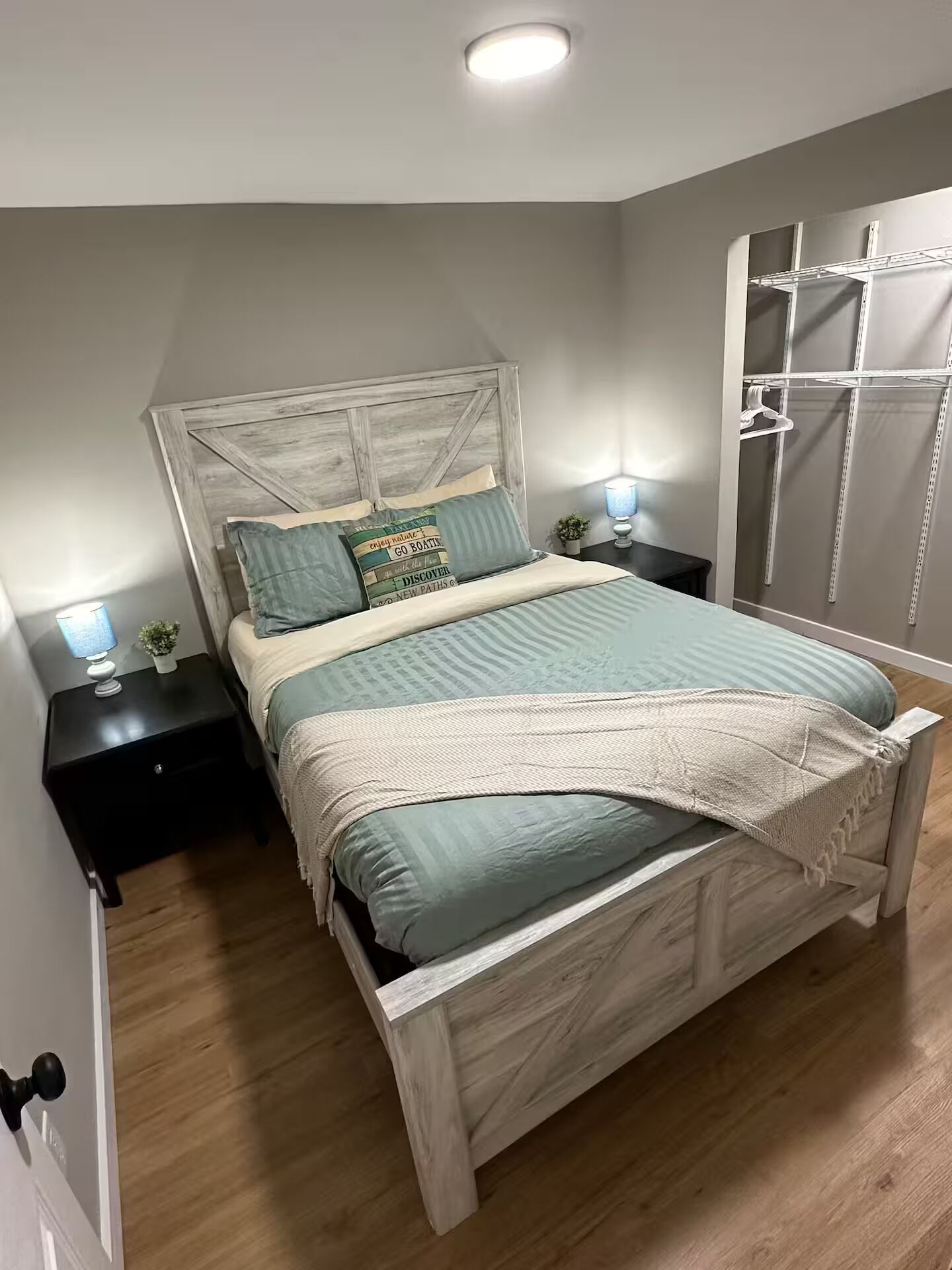 A bedroom with a wooden bed, two bedside tables with lamps, a nightstand, a wall-mounted shelf, and a wardrobe.