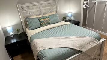 A bedroom with a wooden bed, two bedside tables with lamps, a nightstand, a wall-mounted shelf, and a wardrobe.