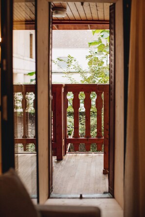 Ein Holzbalkon mit Geländern, Blick auf Grünflächen und ein Gebäude im Hintergrund.