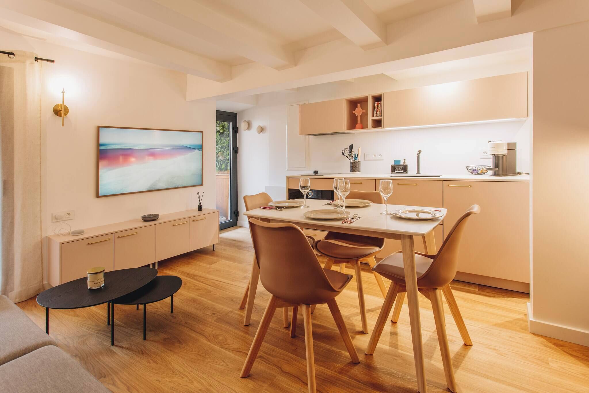 A modern kitchen with wooden cabinets, a dining table set for four, and a large abstract painting on the wall.