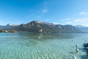 Ein klarer See mit Bergen im Hintergrund und Bojen im Wasser.