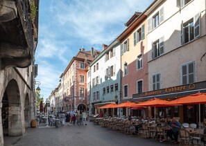 Eine Kopfsteinpflasterstraße gesäumt von bunten Gebäuden, mit Außenplätzen eines Cafés und einem Steinbogen.