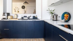 Una cucina moderna con pensili scuri, un piano di lavoro bianco, un lavello, un fornello e una lampada a sospensione.