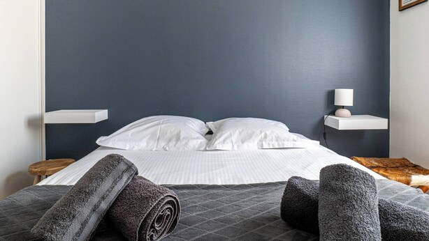 Un letto rifatto con lenzuola bianche, una testata blu scuro e un comodino con una lampada.