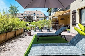 A patio with a lounge chair, potted plants, and a wooden fence. - The Squirrel Garden - Terrace - Parking - Lake (Annecy)