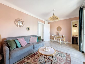 Ein Wohnzimmer mit einer Couch, einem runden Couchtisch, einer Hängelampe und einem Essbereich mit Tisch und Stühlen.
