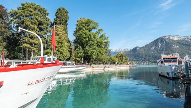 En lystbådehavn med fortøjede både, klart vand og et bjergrigt baggrundsmiljø.