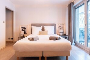 Une chambre d’hôtel avec un grand lit, deux tables de chevet, une fenêtre donnant sur un beau paysage et des œuvres d’art accrochées aux murs.