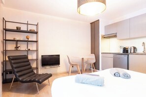 A modern hotel room with a bed, a desk, a chair, a TV, a bookshelf, and a kitchenette. - L'Adresse - City - Annecy (Annecy)