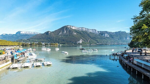 Un lago con barcos, un muelle y montañas al fondo.