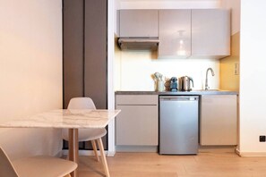A compact kitchen with a dishwasher, a sink, and a stove. There is a dining table with chairs. - L'Adresse - City - Annecy (Annecy)