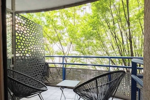 A balcony with two chairs and a small table, a perforated metal partition, and a view of green trees and buildings. - L'Adresse - City - Annecy (Annecy)