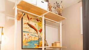 Un dormitorio con cama, cómoda blanca, estante con adornos y un cuadro de pájaros.
