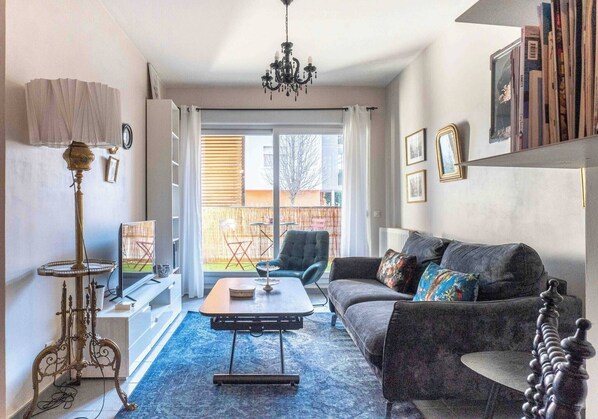 Ein Wohnzimmer mit einer Couch, einem Couchtisch, einem Fernseher, einer Chandelieber und einem Bücherregal.