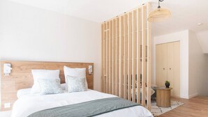 Ein Schlafzimmer mit einem hölzernen Kopfteil, einem Bett mit weißer Bettwäsche, einer grünen Tagesdecke, einer Holzvertäfelung, einem kleinen runden Tisch mit einer Pflanze und einer Pendelleuchte.