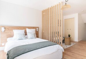 Ein Schlafzimmer mit einem hölzernen Kopfteil, einem Bett mit weißer Bettwäsche, einer grünen Tagesdecke, einer Holzvertäfelung, einem kleinen runden Tisch mit einer Pflanze und einer Pendelleuchte.