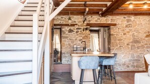 Un loft spacieux avec un mur en pierre, un coin cuisine doté de tabourets de bar et un escalier en bois.
