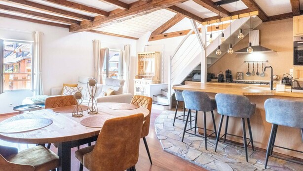 Une cuisine spacieuse avec un plafond en bois, un coin repas avec une table ronde et des chaises, et un escalier menant à un niveau supérieur.