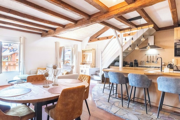 A spacious kitchen with a wooden ceiling, a dining area with a round table and chairs, and a staircase leading to an upper level. - Under the Annecy sky - Pedestrian street - City center - Balcony (Annecy)