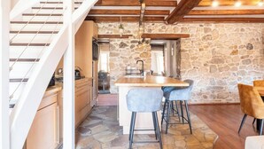 Une cuisine avec un mur en pierre, des poutres apparentes, un îlot central et des tabourets de bar.