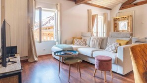 Un salon confortable avec un canapé, une petite table ronde, un téléviseur et une fenêtre avec des rideaux.