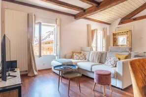 A cozy living room with a sofa, a small round table, a TV, and a window with curtains. - Under the Annecy sky - Pedestrian street - City center - Balcony (Annecy)