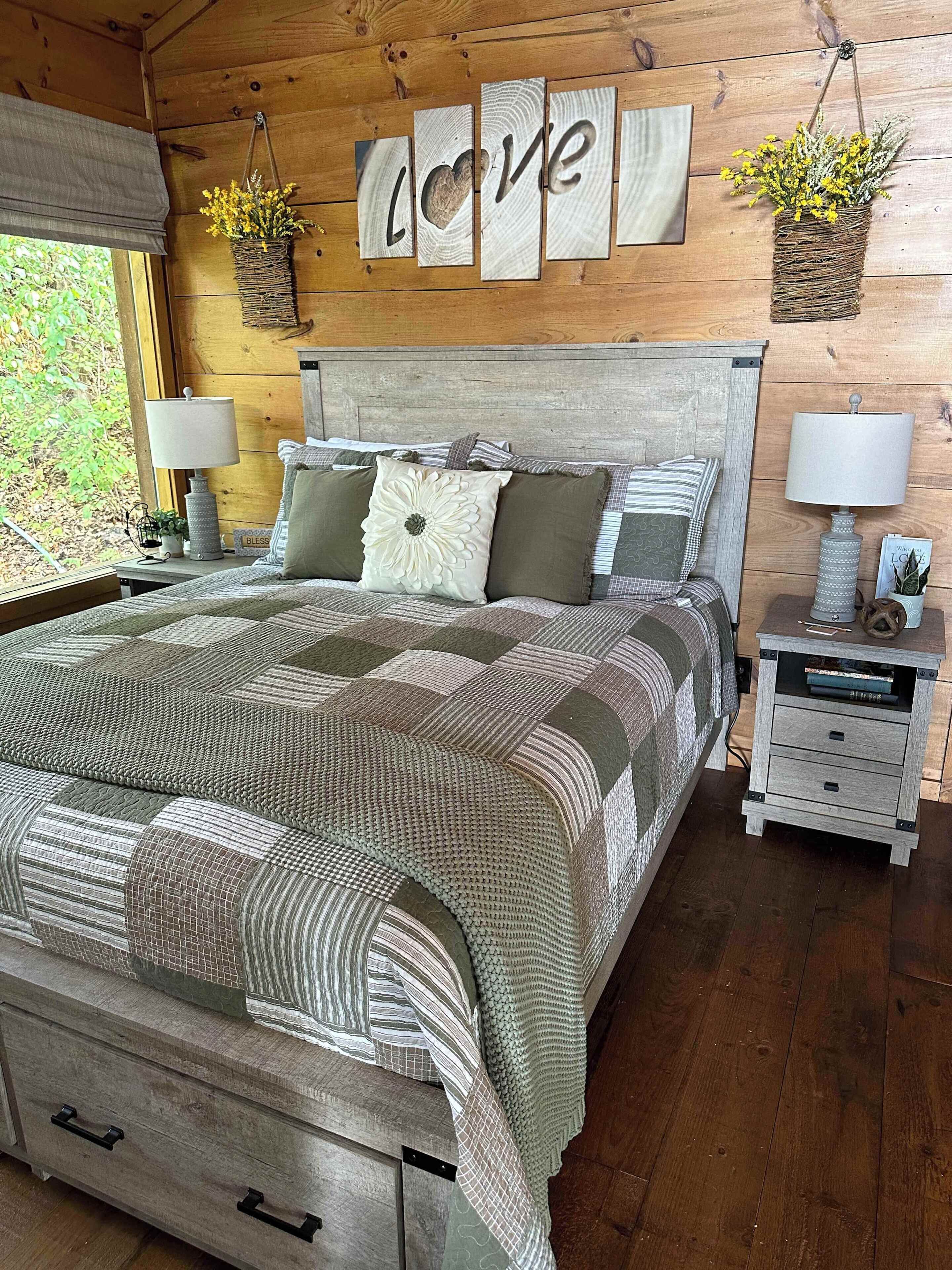 A wooden bedroom with a bed, two bedside tables, a nightstand, and a wall-mounted word 'LOVE'.