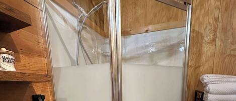 A shower enclosure with a glass door, a towel rack with towels, and a shelf with a container labeled 'Makeup Pallets'.