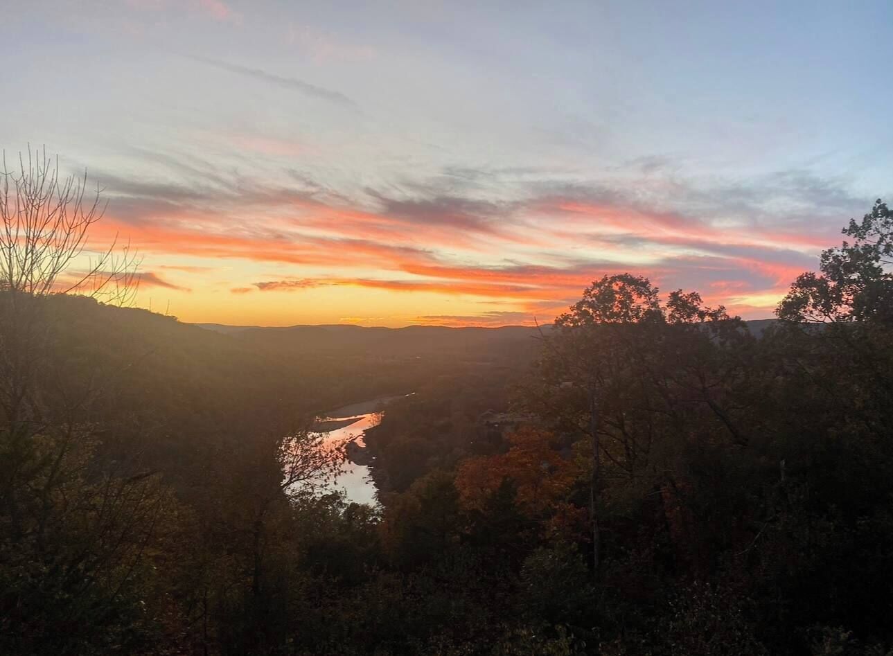 Een landschap met een rivier, bomen en een zonsondergang.
