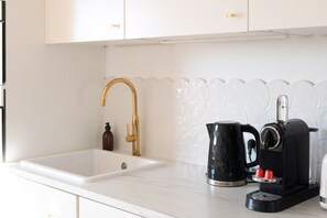 A kitchen with a gold faucet, a black coffee maker, and a kettle on the counter. - LA HAUT - Center annecy- Balcony view lake (Annecy)
